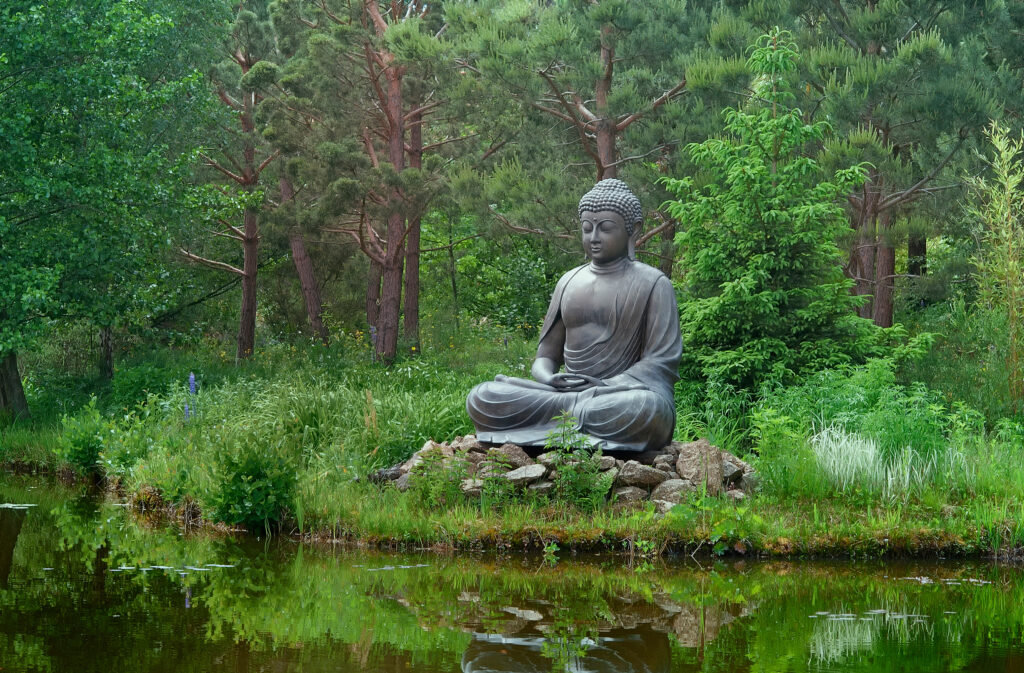 "Statue de Bouddha en méditation au bord d’un étang, entourée d’une nature verdoyante, représentant la sérénité et l’harmonie idéale pour le yoga et la méditation